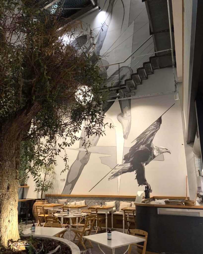 האגורה ב- Ergon House, ברקע ציור הקיר של INO - אומן יווני מפורסם